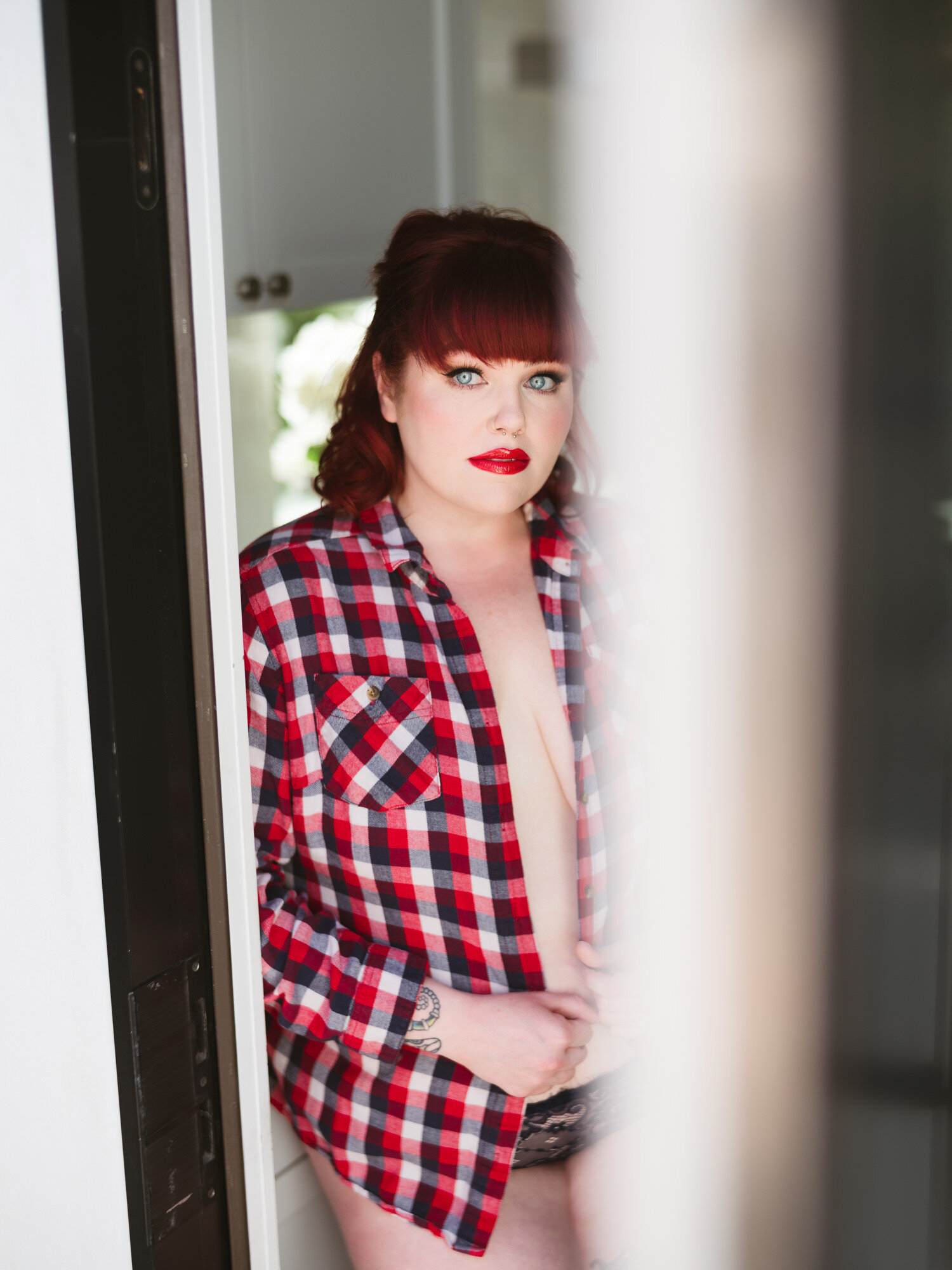 Redhead in a plaid flannel shirt leaning in the studio doorway, casual boudoir portrait