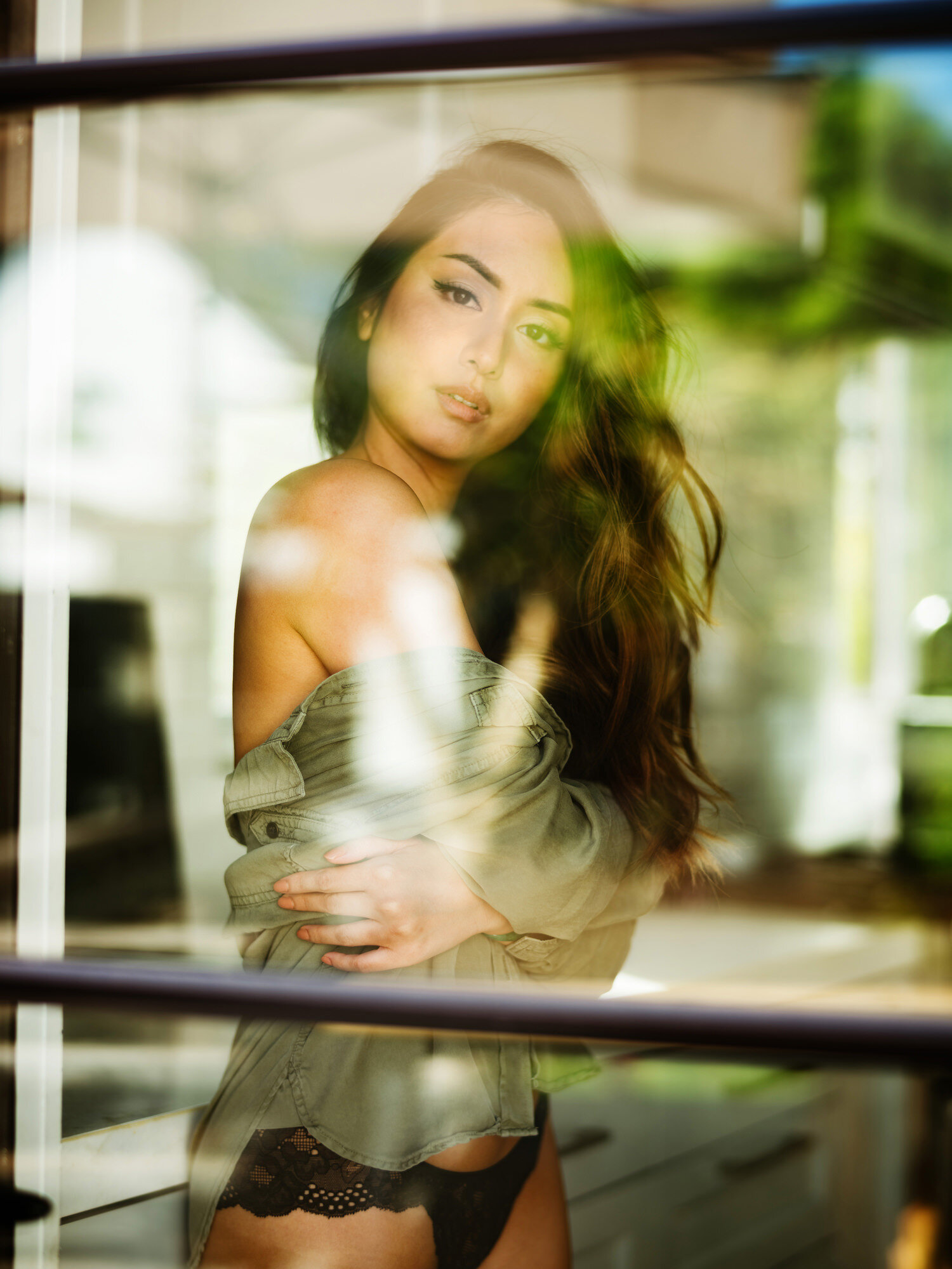 Artistic boudoir portrait through window glass with garden reflections