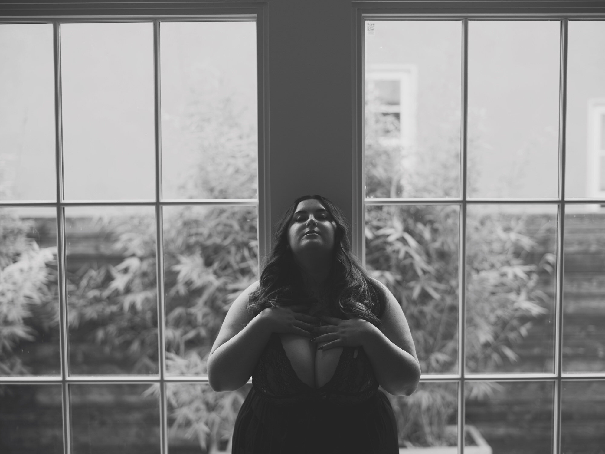 Black-and-white boudoir portrait behind a rain-speckled window