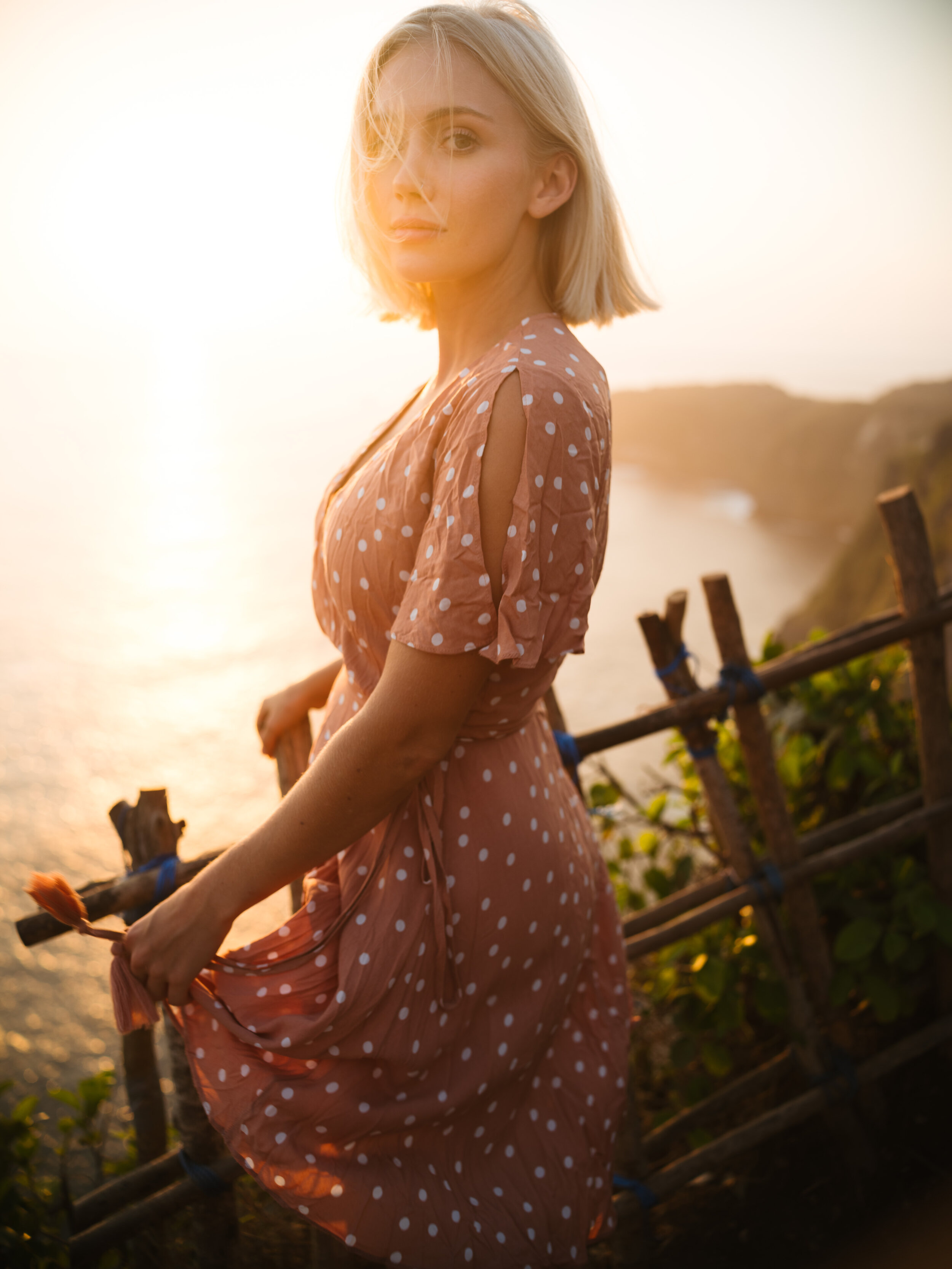 Woman in a floral dress at a lakeside railing at dusk